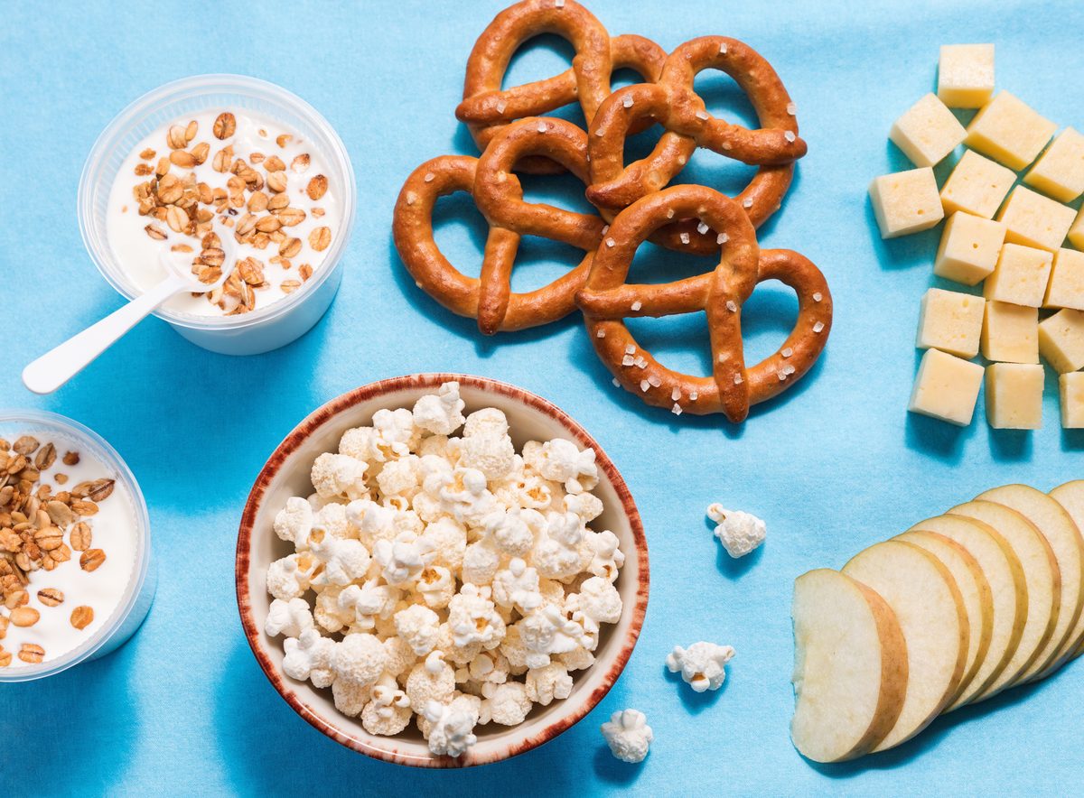Flat-lay of braces-safe snacks including popped sorghum, pretzels, cheese cubes, apple slices, and yogurt
