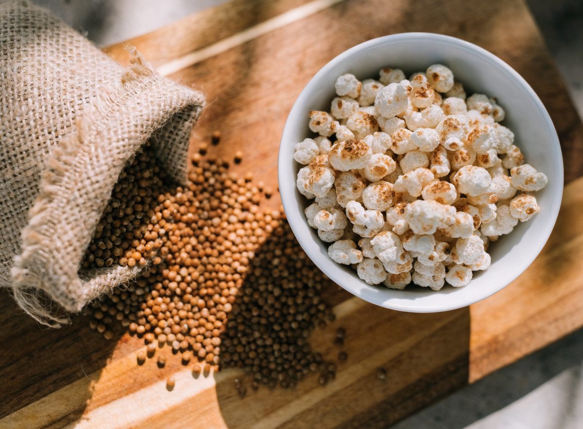 Raw sorghum grain kernels spilling from a burlap sack next to a bowl of freshly popped sorghum